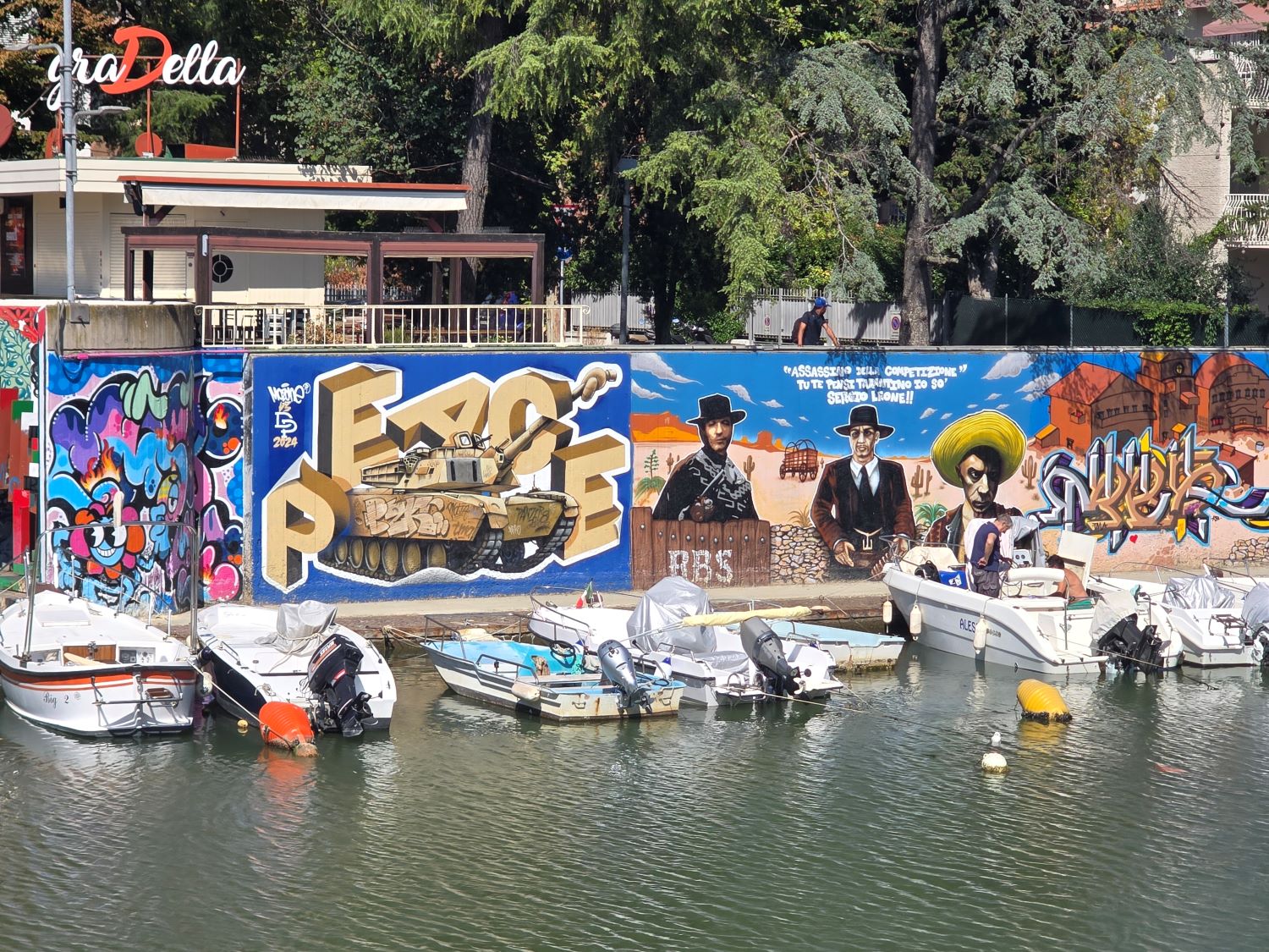 Colourful graffiti mural behind fishing boats on Rimini's canal