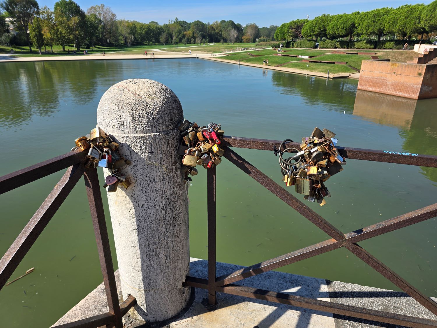Love padlocks on a bridge railing overlooking Rimini's park waterway